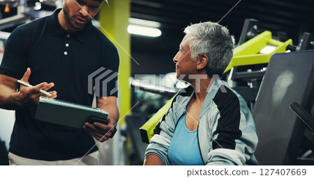 Talking, man and personal trainer with tablet, woman and showing workout progress, fitness and online. Health club, people and explaining training routine to mature client, instructor and tech in gym Talking, man and personal trainer with tablet, woman and showing workout progress, fitness and online. Health club, people and explaining training routine to mature client, instructor and tech in gym 127407669