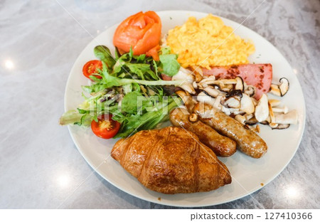 close up of an all day breakfast (English breakfast) with scrambled egg, salad, cherry tomato, smoked salmon, stir fried mushroom, ham, sausage and croissant  127410366