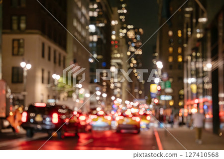 A dreamy blurred photo of Midtown Manhattan shows glowing headlights, taillights, and sparkling city buildings. The soft bokeh effect captures the energy and motion of nighttime traffic. 127410568
