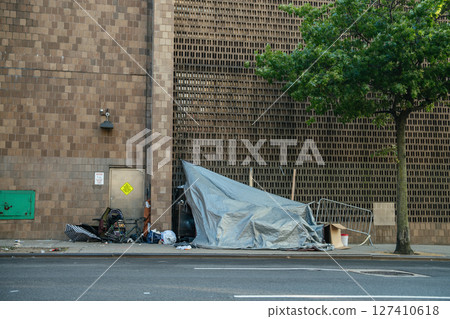 A temporary shelter made of tarps and shopping carts stands against a brick wall in an urban setting. The scene reflects homelessness and the challenges of life on the streets. A temporary shelter made of tarps and shopping carts stands against a brick wall in an urban setting. The scene reflects homelessness and the challenges of life on the streets. 127410618