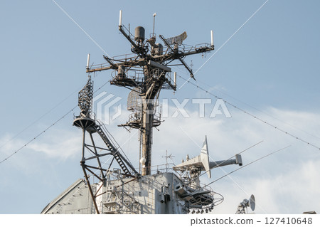 A high-resolution close-up captures the radar mast and antenna array on a historic military aircraft carrier. The intricate metal framework stands out against the soft blue sky. A high-resolution close-up captures the radar mast and antenna array on a historic military aircraft carrier. The intricate metal framework stands out against the soft blue sky. 127410648