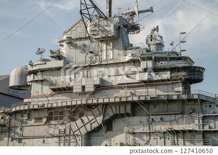 A close-up of the command tower on a historic aircraft carrier shows detailed antennas, satellite dishes, and observation windows. The steel structure reflects military engineering and maritime design 127410650