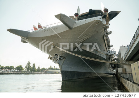 Front view of the USS aircraft carrier showing the massive bow and anchor chains. The historic warship is docked at the pier with a clear view of the surrounding waterfront. 127410677