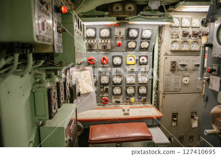A vintage submarine control bench is surrounded by analog meters, switches, and red valve handles. Panels and gauges are used for monitoring power, pressure, and engine status. A vintage submarine control bench is surrounded by analog meters, switches, and red valve handles. Panels and gauges are used for monitoring power, pressure, and engine status. 127410695