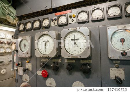 A submarine motor control panel features large analog dials, RPM indicators, and rotary knobs. The panel is part of a complex system used for speed and direction management. 127410713