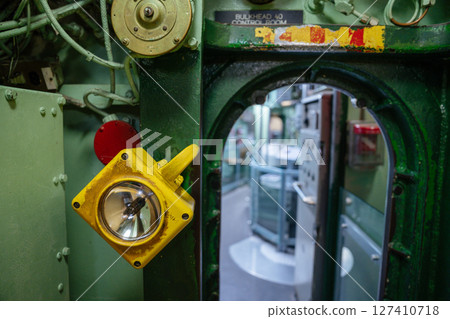 A yellow light is mounted beside a green submarine hatch marked Bulkhead 40 Control Room. The hatch opens into a corridor with visible equipment and control panels inside. A yellow light is mounted beside a green submarine hatch marked Bulkhead 40 Control Room. The hatch opens into a corridor with visible equipment and control panels inside. 127410718