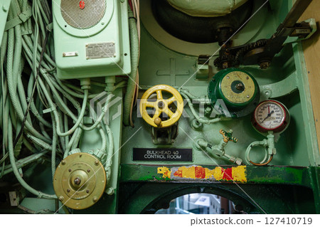 A detailed view of submarine machinery shows yellow and green control valves, a pressure gauge, and thick cables. The control panel is marked as Bulkhead 40 inside the submarine. A detailed view of submarine machinery shows yellow and green control valves, a pressure gauge, and thick cables. The control panel is marked as Bulkhead 40 inside the submarine. 127410719