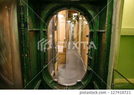 A narrow corridor inside a U.S. Navy submarine is viewed through a green-painted metal hatch. The hallway is lined with doors and bunks, showing the compact layout of the crew area. A narrow corridor inside a U.S. Navy submarine is viewed through a green-painted metal hatch. The hallway is lined with doors and bunks, showing the compact layout of the crew area. 127410721