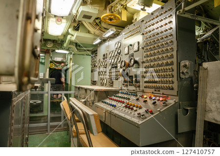 A complex control room inside a historic U.S. Navy submarine is filled with buttons, dials, and gauges. Metal walls and engineering systems reveal the submarine's operation area. A complex control room inside a historic U.S. Navy submarine is filled with buttons, dials, and gauges. Metal walls and engineering systems reveal the submarine's operation area. 127410757