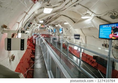 The interior of a preserved U.S. Navy submarine is converted into a museum exhibit with a modern glass walkway. Informational screens and restored mechanical parts line the walls under bright lighting The interior of a preserved U.S. Navy submarine is converted into a museum exhibit with a modern glass walkway. Informational screens and restored mechanical parts line the walls under bright lighting 127410764
