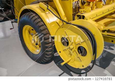 This detailed image shows the large rubber tire and circular cable reel of a yellow utility trailer. The coiled black cable and sturdy industrial design indicate it's part of specialized service This detailed image shows the large rubber tire and circular cable reel of a yellow utility trailer. The coiled black cable and sturdy industrial design indicate it's part of specialized service 127410781