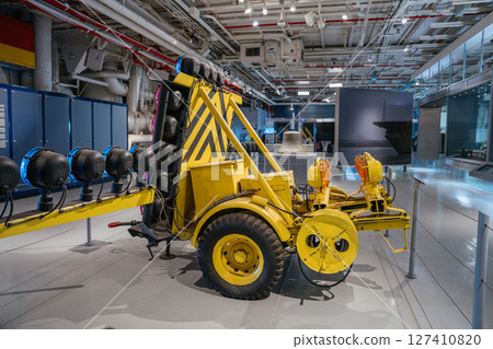 A yellow aviation landing light trailer is displayed indoors with multiple mounted lights and wheels. It is part of a museum exhibit showcasing airport or aircraft carrier guidance equipment. 127410820