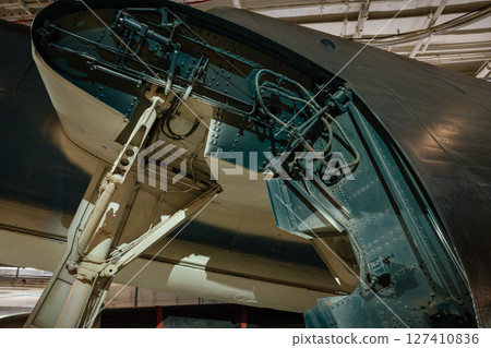 Detailed view of the landing gear and hydraulic systems inside a military aircraft's wheel well. The image shows mechanical components, cables, and structural elements. Detailed view of the landing gear and hydraulic systems inside a military aircraft's wheel well. The image shows mechanical components, cables, and structural elements. 127410836