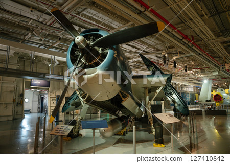 A restored vintage propeller aircraft is showcased indoors with its wings partially folded and a torpedo mounted underneath. The museum lighting highlights mechanical details and historical A restored vintage propeller aircraft is showcased indoors with its wings partially folded and a torpedo mounted underneath. The museum lighting highlights mechanical details and historical 127410842