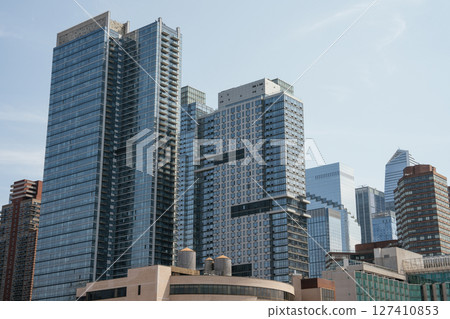 Tall modern skyscrapers with glass facades dominate the cityscape of Midtown Manhattan. The image features a mix of residential and commercial high-rise buildings under a clear sky. Tall modern skyscrapers with glass facades dominate the cityscape of Midtown Manhattan. The image features a mix of residential and commercial high-rise buildings under a clear sky. 127410853