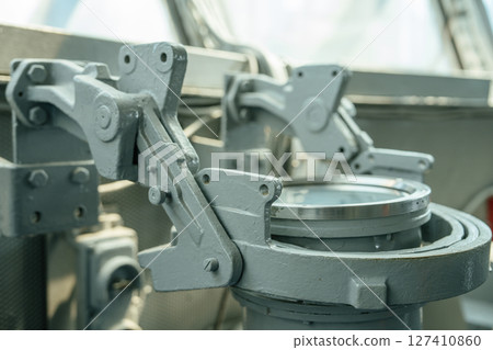 Close-up of a gray metal mount used to secure navigation equipment on a ship's bridge. The sturdy construction features bolts and hinges, designed for heavy-duty marine use. 127410860