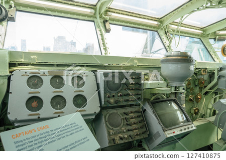 Old naval ship's captain's bridge featuring analog gauges, communication panels, and radar screens. A historic sign explains the captain's role and view from this vantage point. 127410875