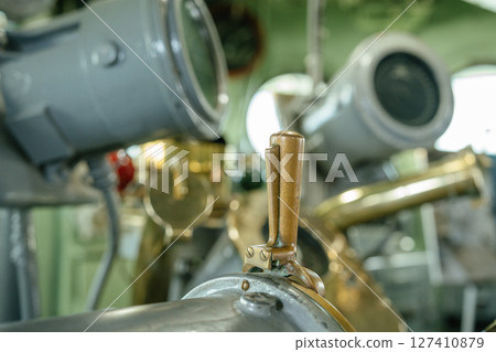 Detailed view of a bronze lever attached to classic ship navigation machinery. The equipment is part of a historic vessel's control room, surrounded by other nautical instruments. 127410879