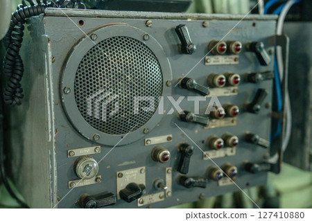 Close-up of a vintage military speaker unit with multiple labeled switches, knobs, and signal indicators. The panel appears to be used for shipboard or secure radio communications. Close-up of a vintage military speaker unit with multiple labeled switches, knobs, and signal indicators. The panel appears to be used for shipboard or secure radio communications. 127410880