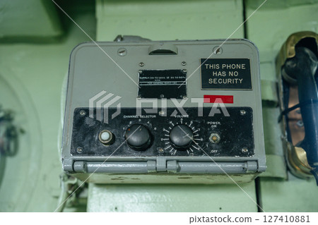 Close-up of a military phone device with a bold label stating This Phone Has No Security. The unit includes channel and volume dials and a handset on the right side. Close-up of a military phone device with a bold label stating This Phone Has No Security. The unit includes channel and volume dials and a handset on the right side. 127410881