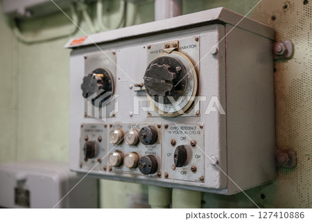 Close-up of an old gyro navigation control panel with labeled dials and switches. The device is mounted on a wall inside a military or naval vessel. 127410886