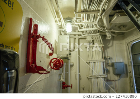 A close-up of a red valve and an empty extinguisher holder on a wall inside a ship's interior. Numerous cables are neatly bundled above, showing an industrial and functional design. 127410890