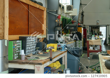 A tidy workbench with small parts drawers and tools is set up in a restoration hangar. Equipment, hoses, and carts fill the background of the organized workspace. A tidy workbench with small parts drawers and tools is set up in a restoration hangar. Equipment, hoses, and carts fill the background of the organized workspace. 127410905