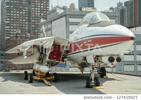 A military fighter jet is parked on a rooftop with buildings in the background. The aircraft is shown in full view, highlighting its landing gear, cockpit, and missile attachment. A military fighter jet is parked on a rooftop with buildings in the background. The aircraft is shown in full view, highlighting its landing gear, cockpit, and missile attachment. 127410925
