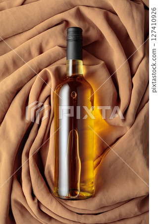 Bottle of white wine against a background of draped beige and brown fabric. 127410926