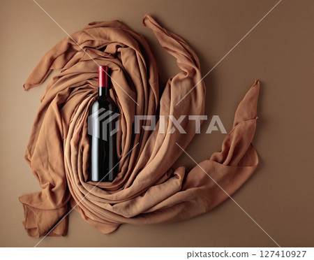 Bottle of red wine against a background of draped beige and brown fabric. Bottle of red wine against a background of draped beige and brown fabric. 127410927