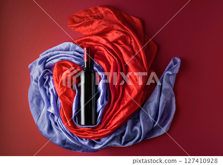 Bottle of red wine against a background of draped red and blue silk fabric. Bottle of red wine against a background of draped red and blue silk fabric. 127410928