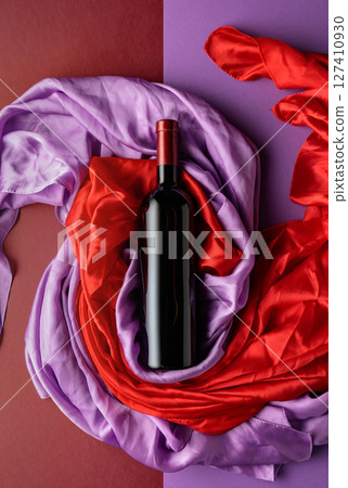 Bottle of red wine against a background of draped red and purple silk fabric. Bottle of red wine against a background of draped red and purple silk fabric. 127410930