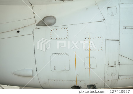 Detailed view of a military aircraft exterior featuring panels, access hatches, and rivets. Visible are drainage streaks and structural elements of the fuselage in clean white paint. Detailed view of a military aircraft exterior featuring panels, access hatches, and rivets. Visible are drainage streaks and structural elements of the fuselage in clean white paint. 127410937