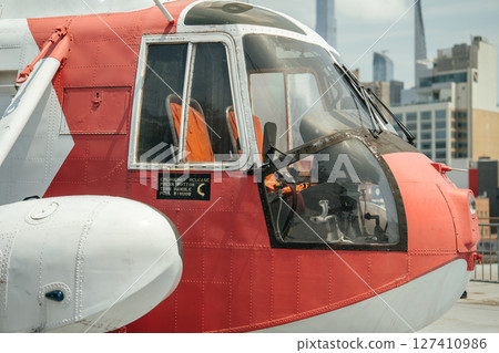Detailed side view of a red and white rescue helicopter showing the cockpit, emergency release sign, and orange seats. The aircraft is part of an outdoor city aviation exhibit. 127410986