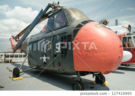 Gray and red military helicopter with number 51 and U.S. Navy markings displayed on an aircraft carrier. The helicopter is parked outdoors in a museum setting under a sunny sky. 127410995