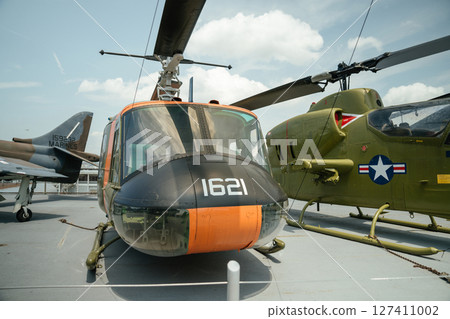Close-up of vintage military helicopters with visible identification numbers and emblems. These aircraft are displayed on the deck of a naval museum ship under a sunny sky. Close-up of vintage military helicopters with visible identification numbers and emblems. These aircraft are displayed on the deck of a naval museum ship under a sunny sky. 127411002