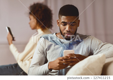 African-american couple ignoring each other, using cellphones on sofa 127411215
