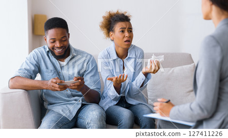 Gadget And Phone Addiction. Frustrated African American Wife Complaining Psychologist About Husband Overusing Cellphone. Selective Focus 127411226