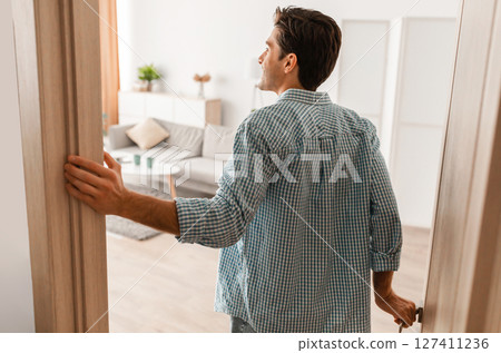 Rear back view of excited young man walking in his apartment, entering new home, happy young guy standing in doorway of modern flat, looking at design interior, coming inside, selective focus Rear back view of excited young man walking in his apartment, entering new home, happy young guy standing in doorway of modern flat, looking at design interior, coming inside, selective focus 127411236