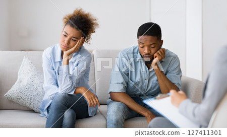 Tired of relationship. Upset african american couple sitting on couch at marital therapist's office. Selective focus 127411301