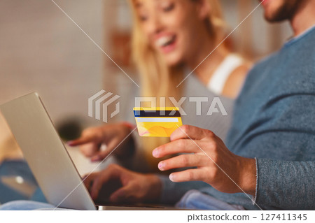 Unrecognizable Couple Using Laptop And Credit Card Shopping Online Ordering Something Sitting On Couch At Home. Selective Focus, Cropped 127411345