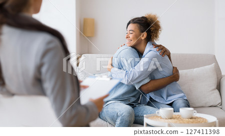 Effective Couples Therapy. Young Afro Husband And Wife Hugging Making Up After A Quarrel At Psychotherapist's Office. Selective Focus Effective Couples Therapy. Young Afro Husband And Wife Hugging Making Up After A Quarrel At Psychotherapist's Office. Selective Focus 127411398