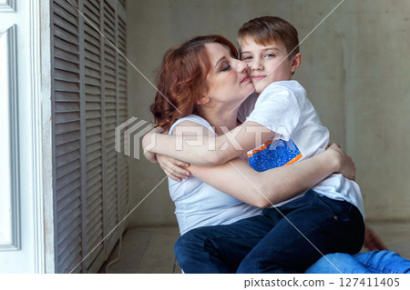 Young mother holding her child. Woman and little boy relax in a bright room. Happy family at home. Young mother playing with her son 127411405