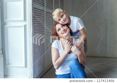 Young mother holding her child. Woman and little boy relax in a bright room. Happy family at home. Young mother playing with her son 127411408
