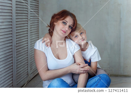 Young mother holding her child. Woman and little boy relax in a bright room. Happy family at home. Young mother playing with her son 127411411