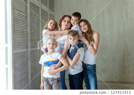 Happy family mother and five children near the wall at home. Woman and little kids relax in a white bedroom. Happy family at home. Young mom playing with their children 127411413