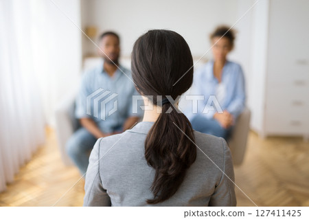 Couples Therapy Session. Counselor Listening To Afro Husband And Wife Sharing Problems In Office. Back View, Selective Focus, Copy Space Couples Therapy Session. Counselor Listening To Afro Husband And Wife Sharing Problems In Office. Back View, Selective Focus, Copy Space 127411425