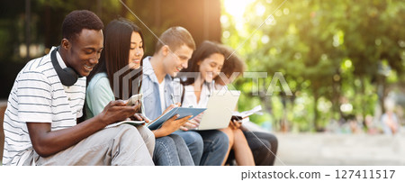 Multiethnic students having fun, studying together for exams outdoors in campus, chatting and smiling during break in classes 127411517
