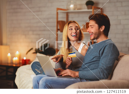 E-Commerce And Online Shopping. Excited Couple Holding Laptop And Credit Card Sitting On Sofa Indoor Buying Things On Internet 127411519