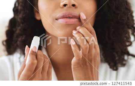 Lip Care. Unrecognizable black woman applying moisturising chapstick on lips, cropped image, closeup 127411543